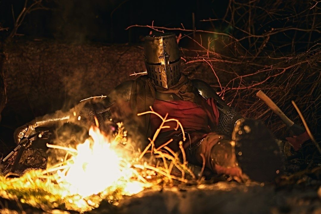 Guerrier médiéval casqué, assis près d’un feu dans une forêt sombre